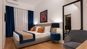 Habitación de hotel moderna con una cama grande, una mesita de noche con lámpara, una silla y un espejo amplio.