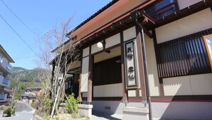 A traditional Japanese building with a tiled roof, wooden beams, and a stone pathway leading to the entrance. - Minshuku Unzen (Unzen)