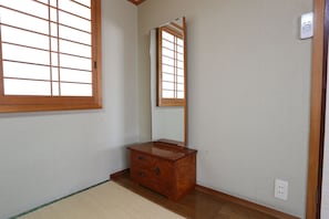 A room with a wooden dresser, a mirror, a window with a grid pattern, and a light switch on the wall. - Minshuku Unzen (Unzen)