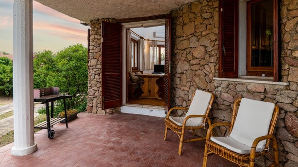 Un portico con pareti in pietra, sedie in vimini, un tavolo e un barbecue.
