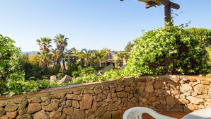 A stone wall, a white plastic chair, and a wooden pergola.