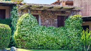 A stone building with a tiled roof, surrounded by well-maintained hedges and a grassy lawn.