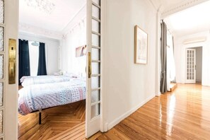 A spacious room with a large bed, a wooden floor, and a door leading to another room.