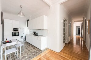 A modern kitchen with white cabinetry, a built-in oven, and a coffee machine.