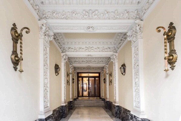 A grand hallway with ornate white and gold detailing, marble flooring, and classical columns.