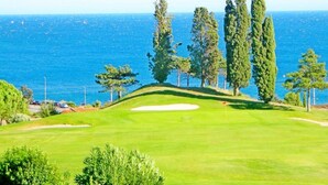 A golf course with a view of the sea and tall trees.