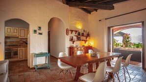 A kitchen with a dining area, featuring a wooden table and chairs, a small island, and a view through a window.