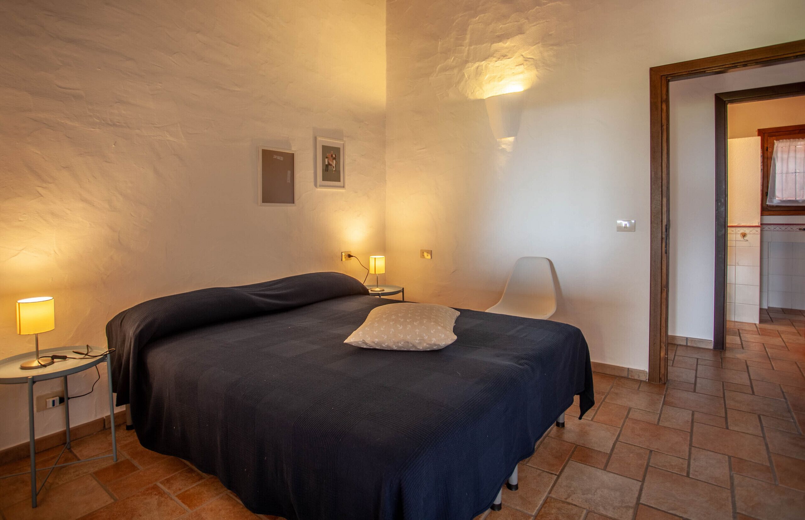 Ein Schlafzimmer mit einem Bett, zwei Nachttischen mit Lampen, einem Sessel und einer Tür zum Badezimmer.