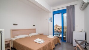A hotel room with two beds, a small table, a chair, a balcony with a view, and a refrigerator. - Agios Pavlos Hotel (Agios Vasileios)