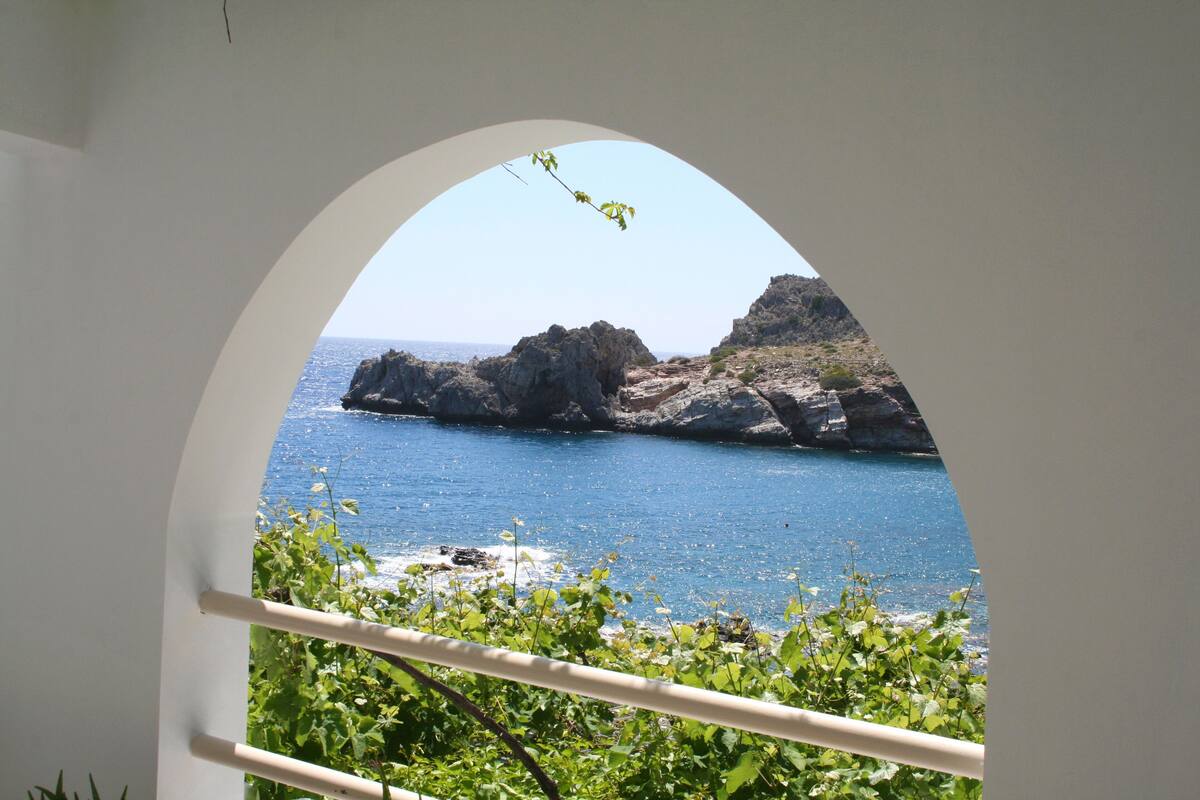 A view through an arched window of a coastal landscape with rocky formations and clear blue water.