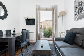 A modern living room with a dining area, a sofa, a coffee table, a TV, and a balcony with a city view.