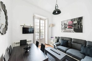 A modern living room with a dining area, a sofa, a TV, and a large window.