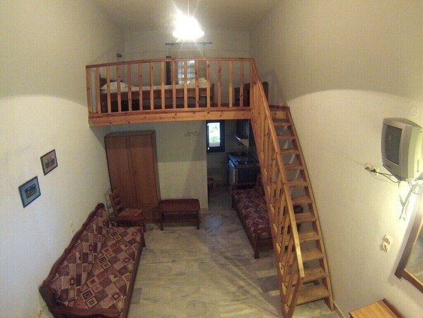 A compact room with a loft bed, a wooden ladder, a sofa, and a television. - Kavos Melissa Studios (Agios Vasileios)