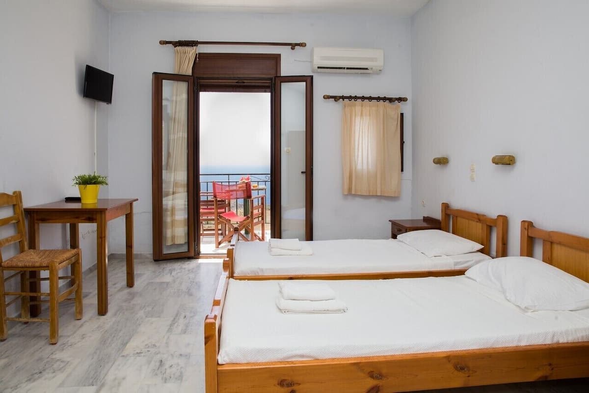 A hotel room with two wooden beds, a small table with a chair, a TV, and an air conditioning unit.