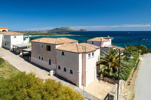 A coastal residential area with terracotta-roofed buildings, a clear blue sky, and a view of the sea.