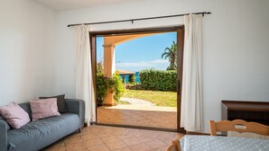 Quarto com sofá, mesa e vista para um jardim e um prédio azul através de uma porta de vidro deslizante.