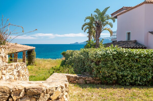 A coastal property with a stone wall, a small building with a tiled roof, and a lush green hedge.