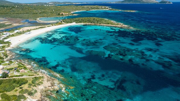 Vista aérea de uma área costeira com águas turquesa cristalinas, uma praia de areia e vegetação ao redor.