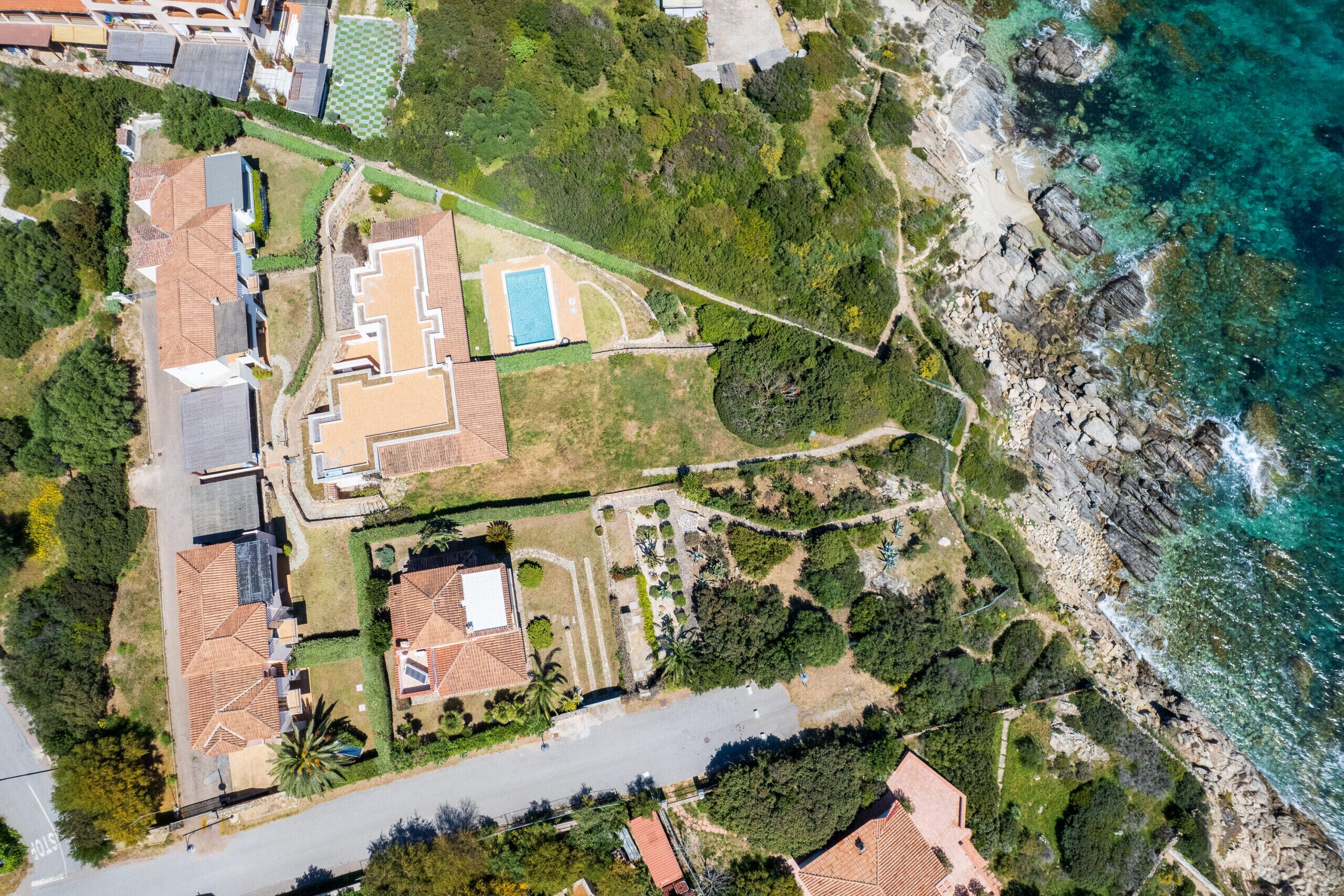An aerial view of a coastal property with a swimming pool, multiple buildings, and a rocky shoreline.
