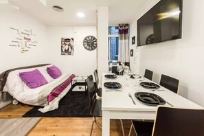 A compact room with a bed, a dining table set for two, and a TV mounted on the wall. - TET (Madrid)