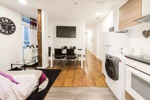 A compact living space with a bed, a dining area, a kitchen, and a wall-mounted TV. - TET (Madrid)