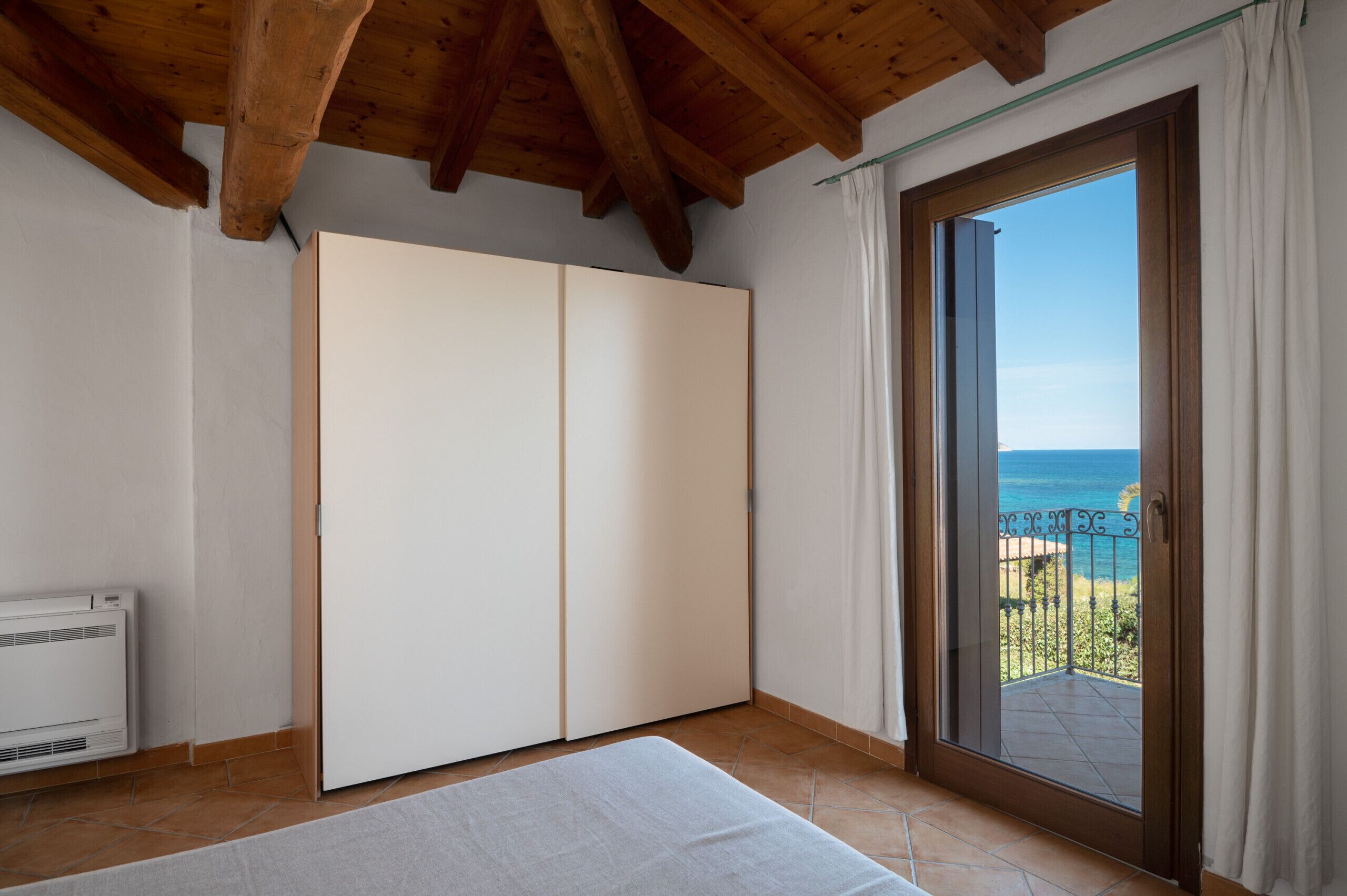 Ein Zimmer mit Schiebeglasfenster zum Balkon, einem weißen Kleiderschrank und einer weißen Heizung.