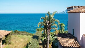 Une vue sur la côte, avec une mer bleue et limpide, un palmier et un bâtiment doté d’un toit en tuiles.