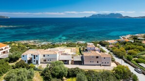 Une zone résidentielle côtière caractérisée par des bâtiments blancs, une mer d’un bleu limpide et un paysage montagneux en arrière-plan.