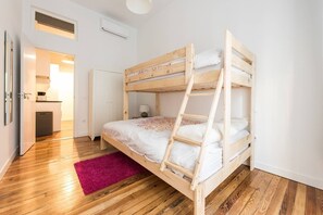 Ein Stockbett in einem Zimmer mit Holzdielen, einem rosafarbenen Teppich und einer weißen Tür, die in einen Küchenbereich führt.