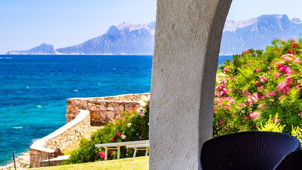 Un patio vista mare e montagne, con un muro in pietra, una sedia in vimini.