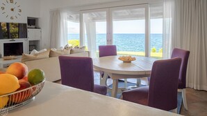 Un'area pranzo con tavolo e sedie, una ciotola di frutta e vista mare.