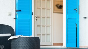 Una stanza con due porte blu, una bianca e una sedia in vimini.