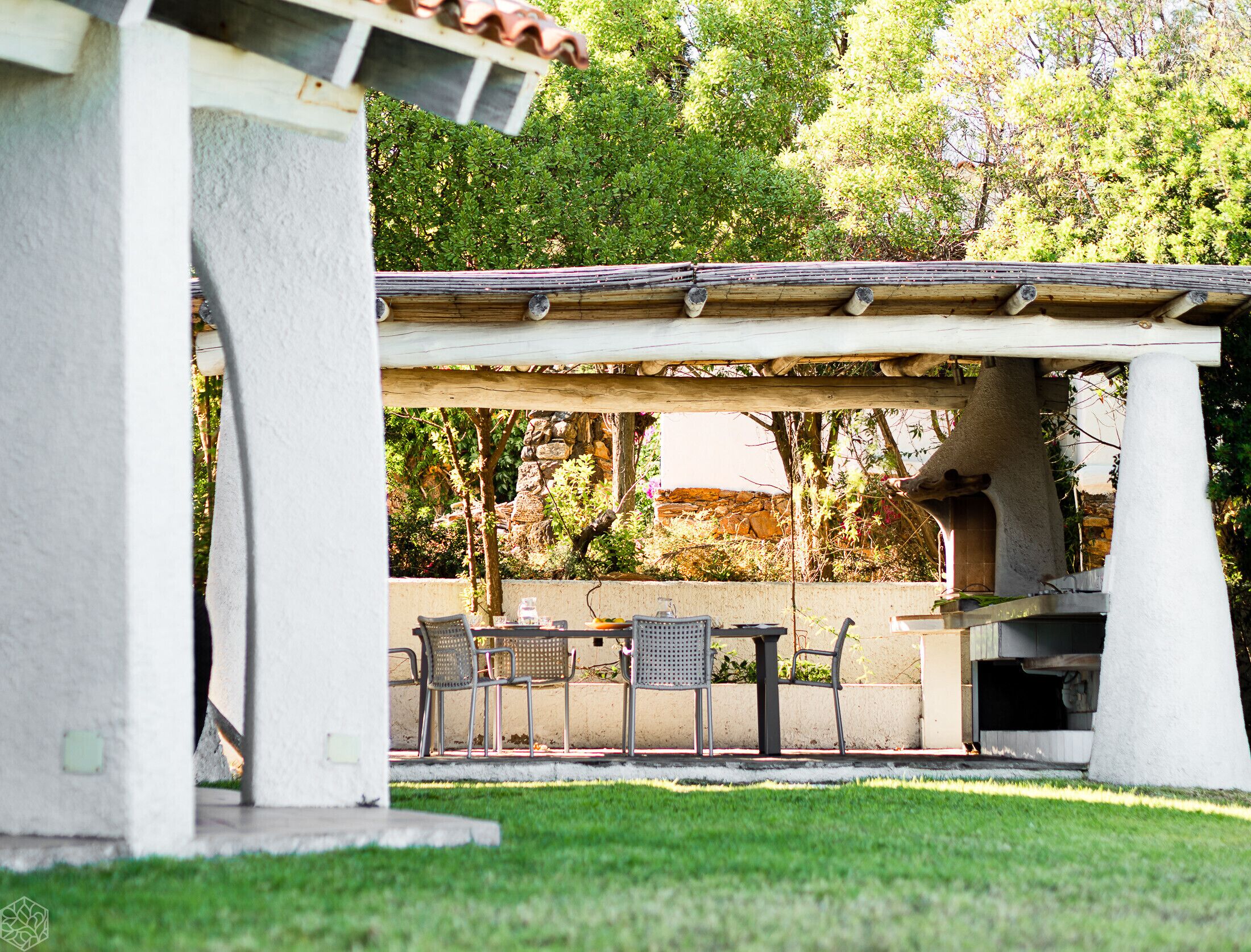Een terras buiten met een pergola, een zitgedeelte en een stenen muur op de achtergrond.