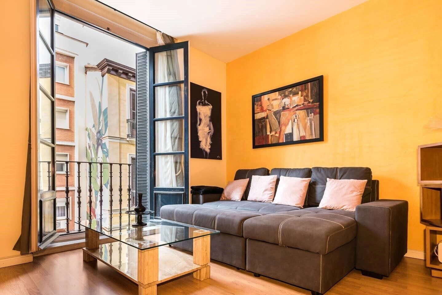 A living room with a glass coffee table, a dark sofa, and a painting on the wall.