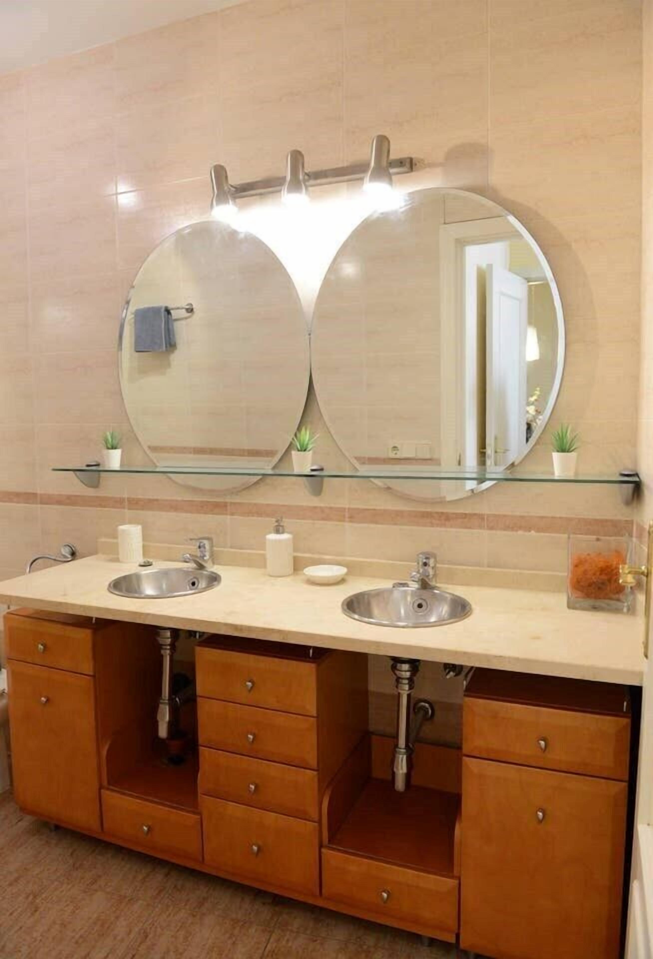 Un baño con dos lavamanos, un espejo doble y un estante de vidrio arriba.