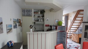 Una cocina compacta con una isla central, una zona de comedor con sillas rojas y una escalera que sube a un nivel superior.
