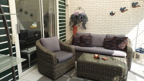 Un patio con muebles de mimbre, una mesa de vidrio y un muro de ladrillo.