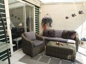 A patio area with wicker furniture, a glass table, and a brick wall.