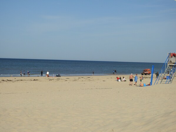 A beach with people walking and sitting, a lifeguard tower, and a clear sky.