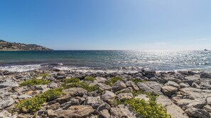 A rocky shoreline with clear blue sea and distant land.