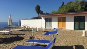 Ein Gebäude am Strand mit einer Tür, einem kleinen Tisch und einem Stuhl.