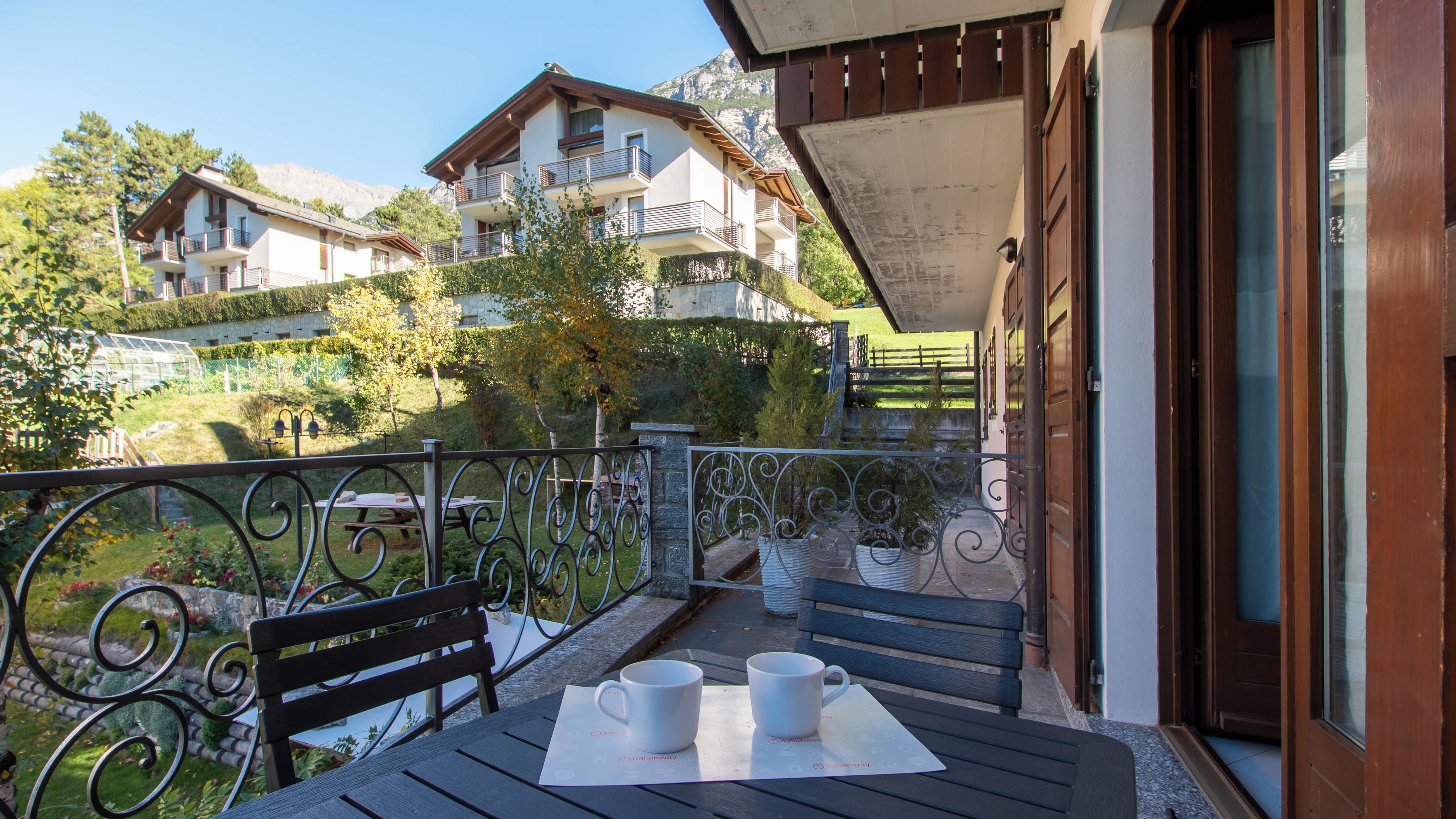 A balcony with two tables, each with a white mug and a placemat.