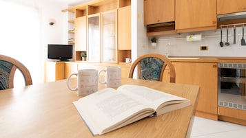 Une cuisine moderne avec des meubles en bois, une table à manger avec deux tasses blanches et un livre ouvert, et un téléviseur en arrière-plan.