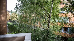 A view of a tree-lined courtyard with a brick building and a balcony.