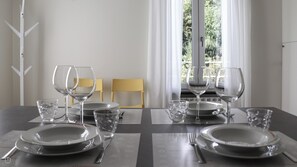 A dining table set with plates, glasses, and cutlery, chairs, and a window with curtains.