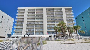 Un hotel de varios pisos con balcones, una playa arenosa al frente y palmeras.