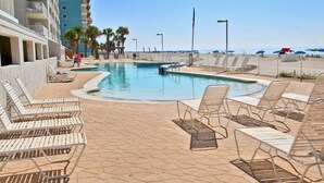 Una piscina con sillones de descanso, vista a la playa y un edificio alto al fondo.