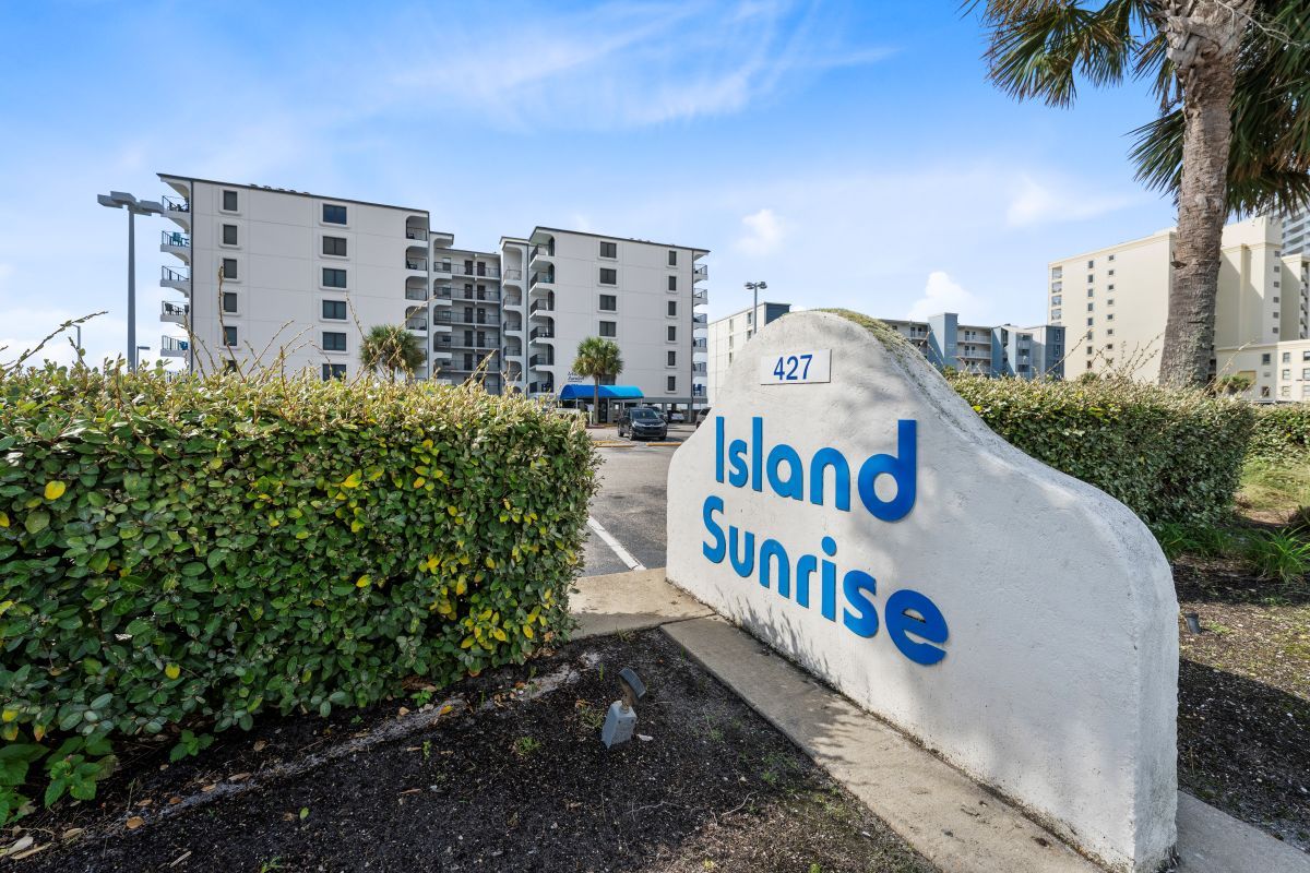 Een bord met de tekst 'Island Sunrise', met een gebouw op de achtergrond.