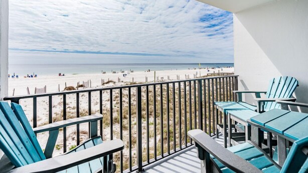 A balcony with a view of the beach, featuring wooden chairs and a table. - Cozy Gulf Front Condo With Beach Front View | Beach Access | Pool | Sleeps 6 (Gulf Shores)
