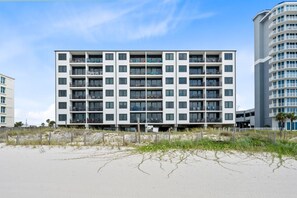 Een hotel met meerdere verdiepingen en balkons, nabij een zandstrand.